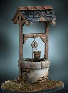 an old fashioned water fountain is displayed on a table with rocks and grass around it