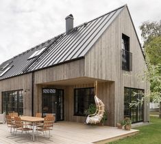 a wooden deck with chairs and tables on it next to a house that has a metal roof