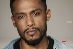 a close up of a person with a beard and blue shirt in front of a gray background