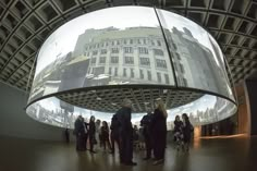 people are standing in front of a large glass sculpture that is reflecting the city's buildings