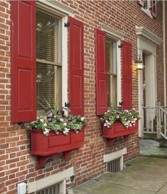 two red window boxes with flowers in them on the side of a brick building,