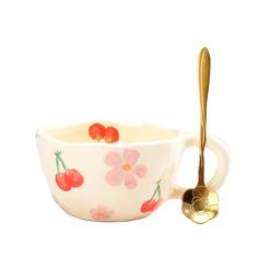 a white bowl with cherries on it and a gold spoon in front of it