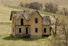 an old abandoned house sitting in the middle of a field with no grass on it