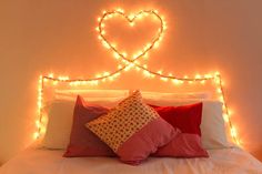 a white bed topped with lots of pillows under a heart - shaped light headboard