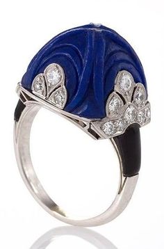 An Art Deco platinum and enamel ring with lapis lazuli and diamonds attributed to Marchak. Set with a carved sugar loaf cut lapis lazuli stone in a classic Art Deco motif and 22 round miligrain set diamonds, further enhanced by the enamel shoulders. Circa 1920's. #Marchak #ArtDeco #ring Luxury Art Deco Cabochon Rings, Blue Cabochon Art Deco Rings, Vintage Lapis Lazuli Jewelry, Chain Maille, Art Deco Jewelry Rings, Luxury Blue Art Nouveau Jewelry, Luxury Vintage Lapis Lazuli Jewelry, Bijoux Art Nouveau, Vintage Cocktail Ring