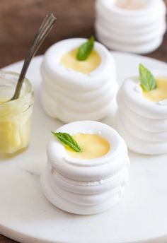 four small white cakes sitting on top of a table next to a jar of yellow liquid