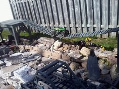 an outdoor area with rocks, chairs and a batman figure on the ground next to a fence