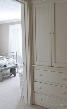 an empty bedroom with white closets and drawers in the corner, next to a bed