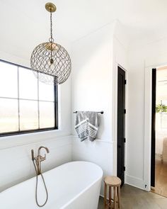 a white bath tub sitting under a window next to a wooden stool in a bathroom