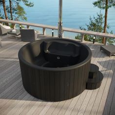 an outdoor hot tub sitting on top of a wooden deck next to the ocean and trees