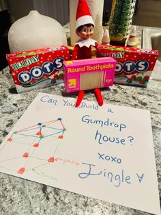 an elf is sitting on the counter next to some gumdrops and a sign that says, can you build a gumdrop house?