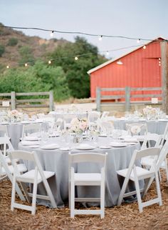 an outdoor table set up with white chairs and silver linens for a wedding reception