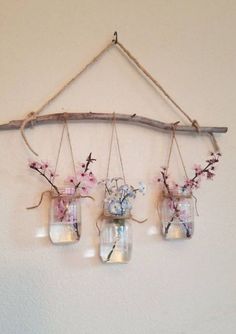 three mason jars with flowers hanging from a branch on the wall, one is filled with water