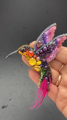 a hand holding a tiny colorful bird brooch