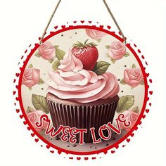 a cupcake with pink frosting and roses on it is hanging from a sign