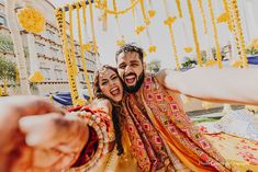 two people standing next to each other in front of a yellow and orange backdrop with flowers