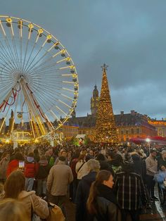 a large group of people standing in front of a ferris wheel and christmas tree at night