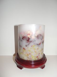 a white candle sitting on top of a red stand next to a white wall and floor