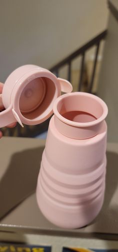 two pink cups sitting on top of a table next to each other, one being held up