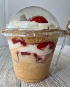 a dessert in a plastic container with whipped cream and cherries on top, sitting on a wooden table