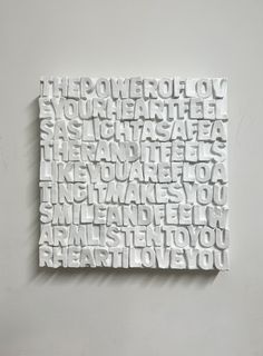 a white sculpture with words written on it in cursive writing, against a gray wall