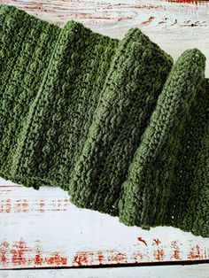 three crocheted green scrubcloths sitting on top of a white wooden table