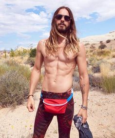 a man with long hair and no shirt standing in the desert