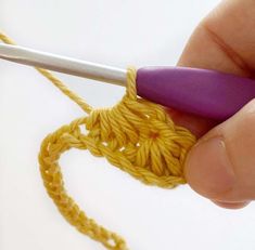 someone is crocheting the end of a piece of yellow yarn with a purple crochet hook