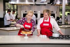 two women in red aprons preparing food on top of a counter next to each other