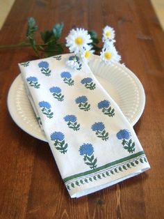 two napkins sitting on top of a white plate next to daisies and green leaves