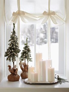 some candles are sitting on a table in front of a window with snow and trees