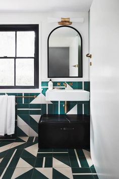 a bathroom with green and white tiles on the floor, black suitcase in the foreground