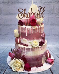 a three tiered cake with flowers and the word shaba on top is sitting on a wooden table