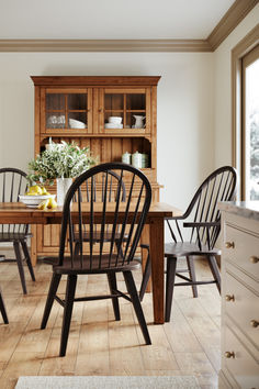 a dining room table with chairs and a hutch in the back ground, next to a window