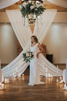 a woman standing in front of a white drape with candles and flowers on it