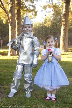 two children dressed up in costumes standing next to each other on grass with trees in the background