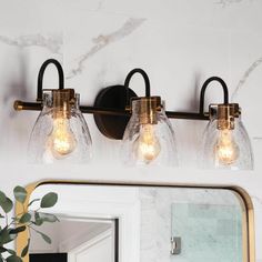 three light bathroom fixture with clear glass shades and gold accents on a marble countertop