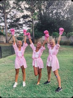 three women in pink outfits are holding up their hands and posing for the camera while standing on grass