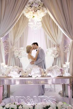 a bride and groom kissing in front of a white couch with flowers on the table