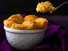 a close up of a spoon with food in it near a bowl on a purple cloth