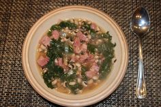 a bowl of soup with meat, beans and spinach on a table next to a spoon