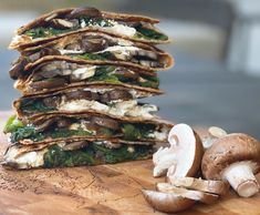 a stack of flatbreads with mushrooms and spinach on a wooden cutting board