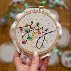 someone is holding up a small embroidery hoop with the word joy written on it in black and white