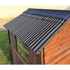 a small wooden building with a metal roof and windows on the side of it, next to a grassy area