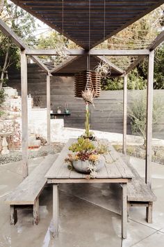 a wooden table with plants on it under a covered area in the back yard,