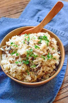 a wooden bowl filled with rice and mushrooms on top of a blue towel next to a wooden spoon