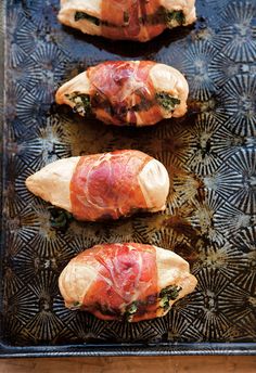 three pieces of meat wrapped in bacon on top of a baking sheet with other food items