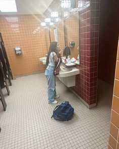 a woman standing in front of a bathroom mirror next to a bag on the floor