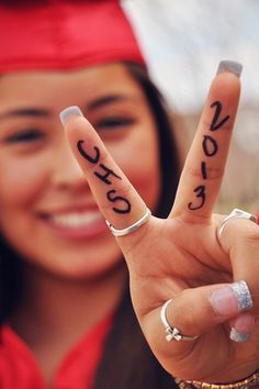 a woman in graduation cap and gown holding up two fingers with the word peace written on them