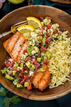 a wooden bowl filled with rice and salmon next to lemon wedges on a blue table cloth